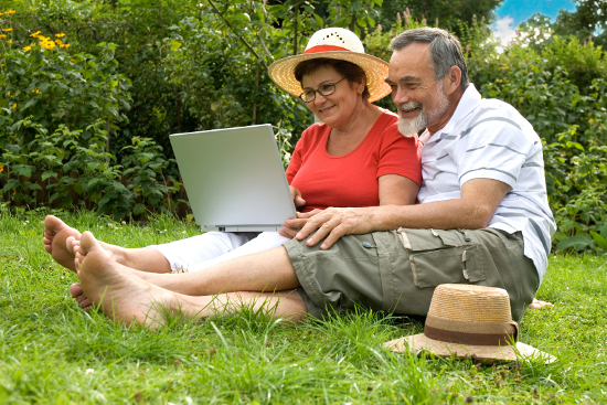 A happy couple of seniors lounging in the grass with a laptop