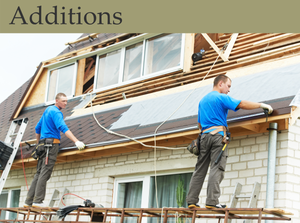 Two workers add roofing to a second story room addition